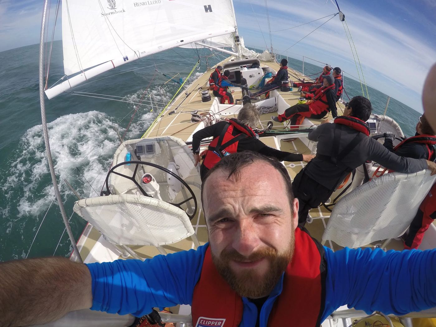 Daniel at the helm of a sailing yacht, grinning into the camera